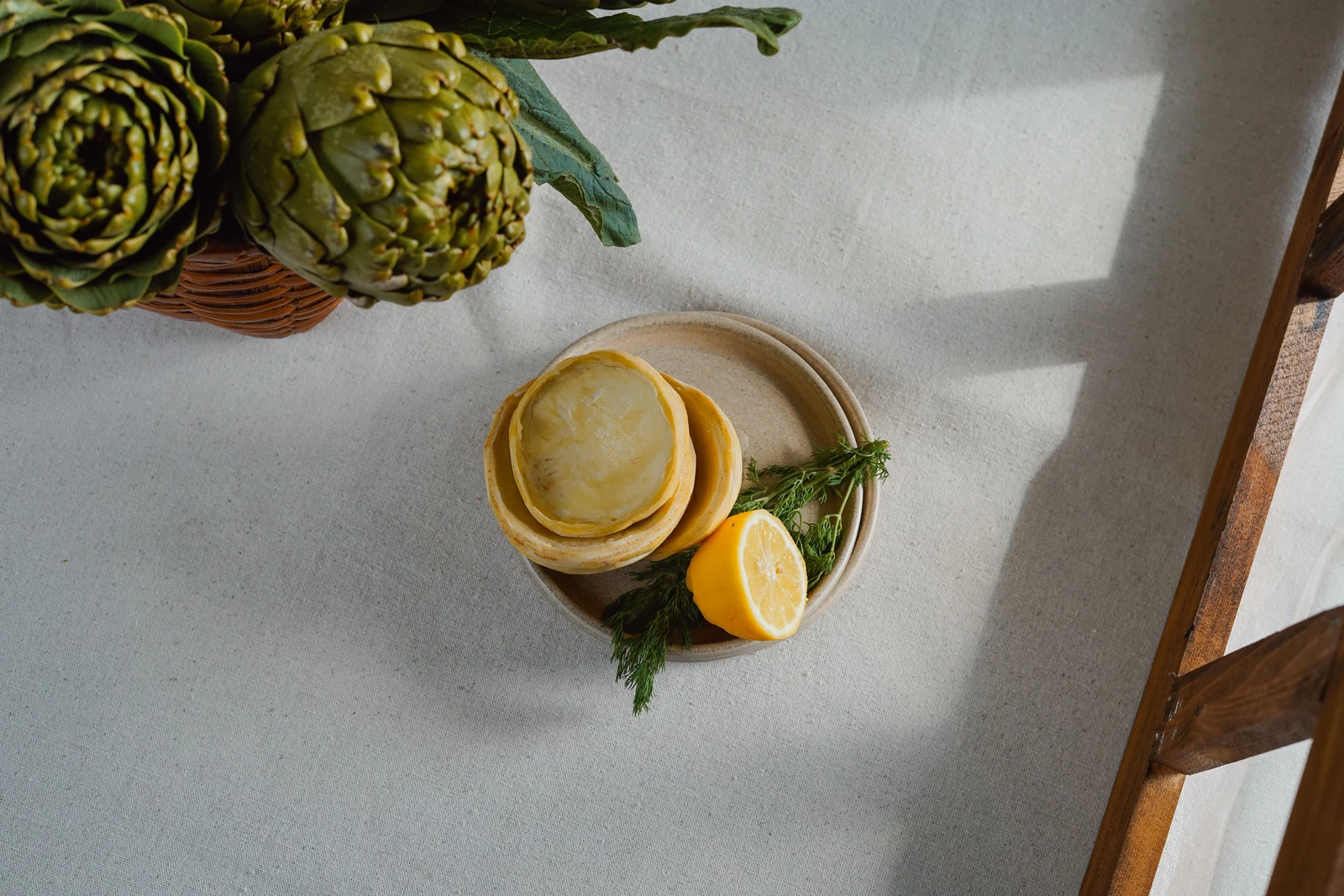 Trimmed artichoke bottoms on a plate with lemon and dill, beside whole artichokes