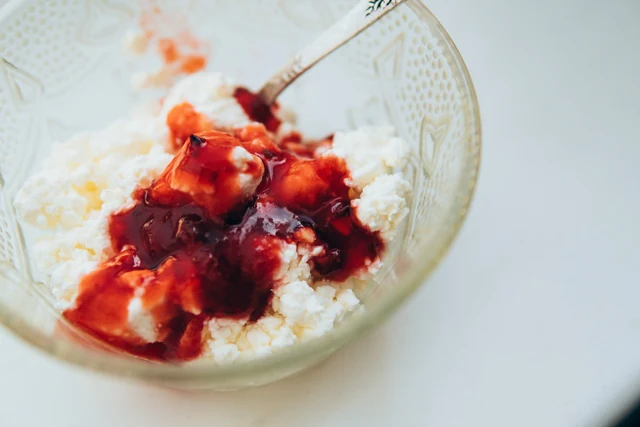 Crumbly white cheese with red fruit preserves in a glass bowl and a spoon