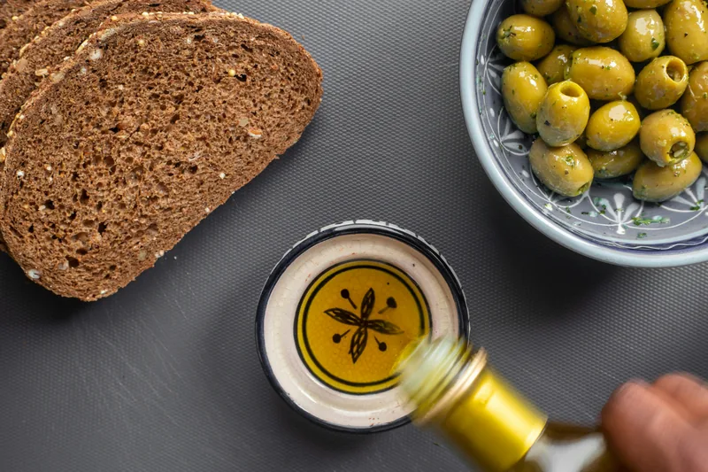 Ekmek ve yeşil zeytinlerin yanında bir kâse zeytinyağı