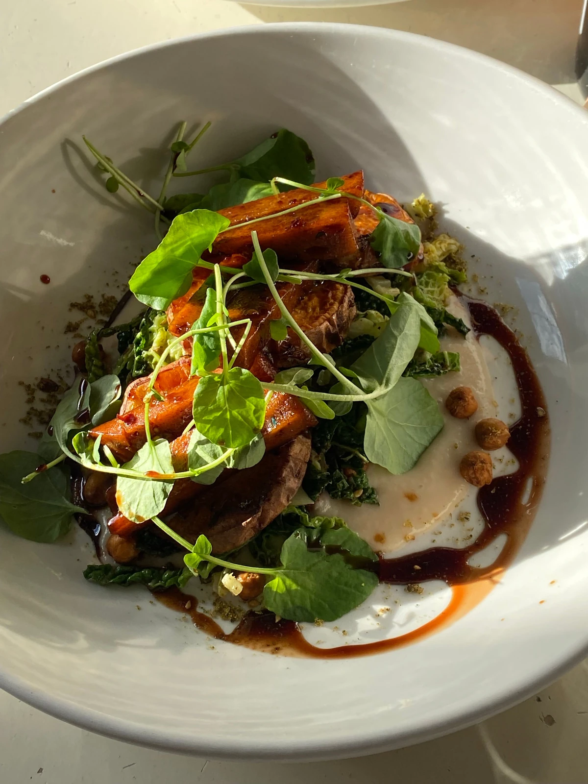 Roasted vegetables and fresh greens on a cream plate with a dark dressing